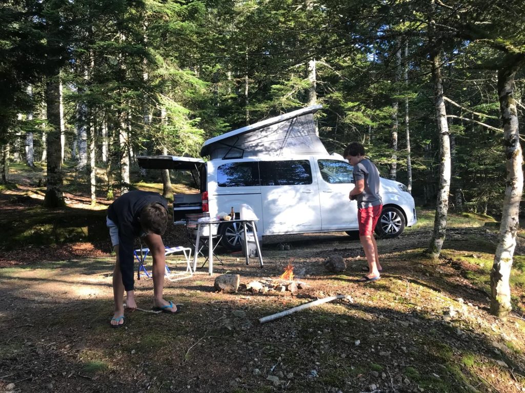Bivouac en van aménagé en forêt, le soir, près d'un feu